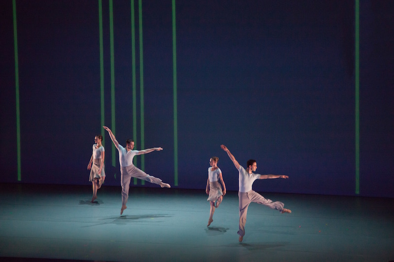 Two men jump into the air on one leg and the other outstretched. Two women in between them also jump off one leg while their other foot is positioned behind their knee